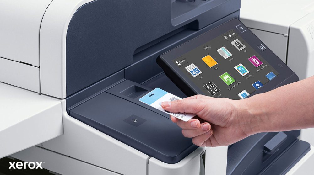 Xerox® Workplace Cloud e Suite: autenticazione sicura e interfaccia intelligente Una mano tiene una tessera di sicurezza e la scansiona vicino al lettore di una moderna stampante multifunzione Xerox, dotata di un ampio display touchscreen che mostra varie icone di applicazioni.